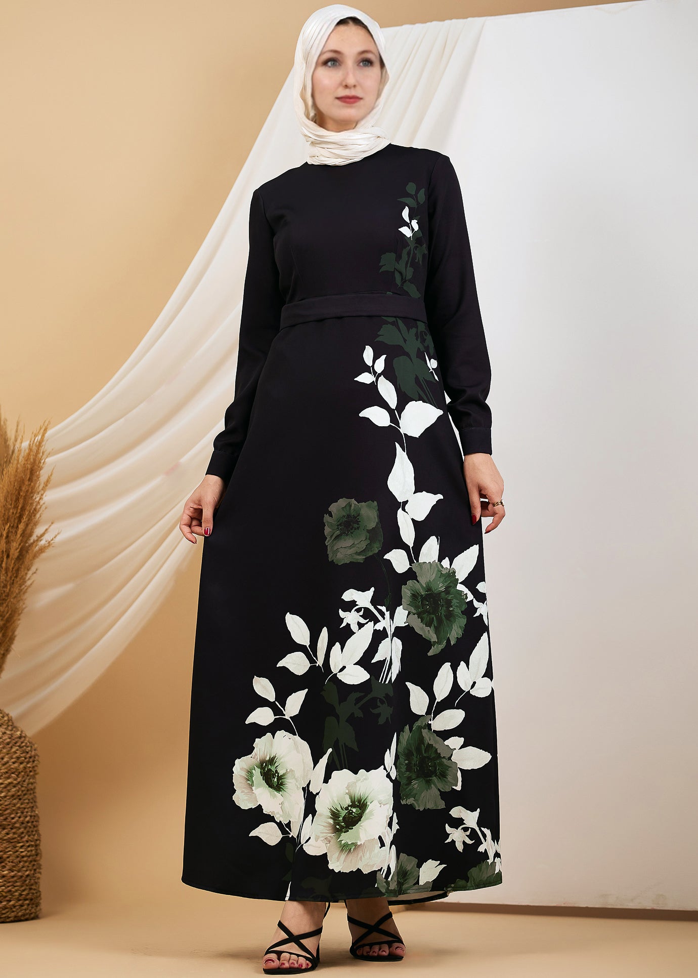 Elegant woman in a black floral maxi dress with green and white leaf accents, front view.