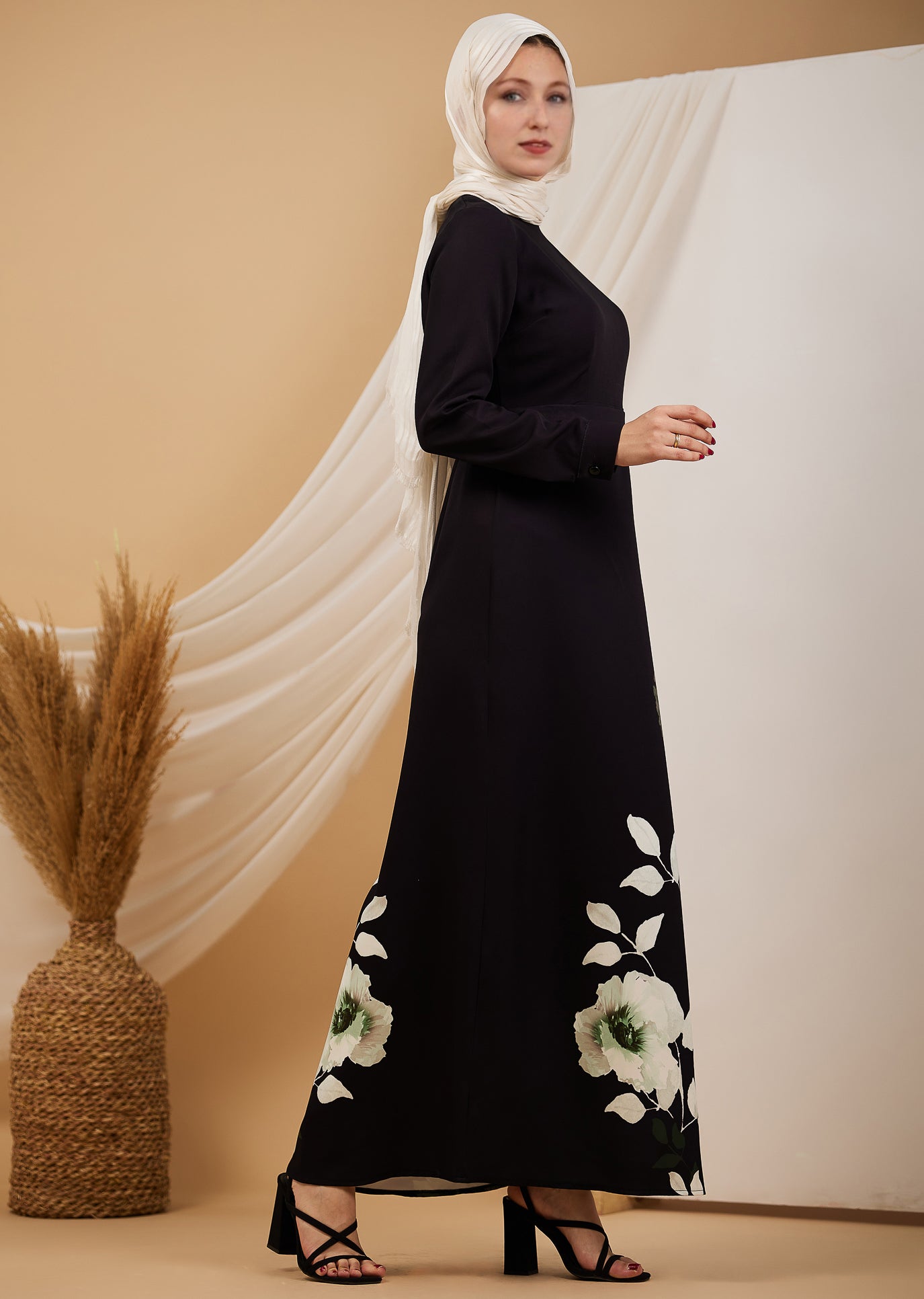 Side view of a black maxi dress with green and white floral designs, worn by a woman in a hijab