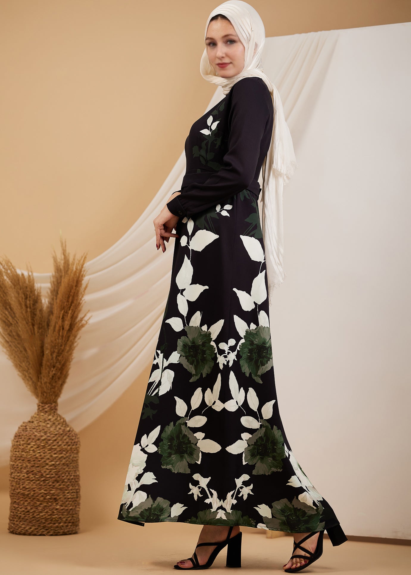 Full front view of a woman wearing an elegant black floral maxi dress, with green and white leaf accents