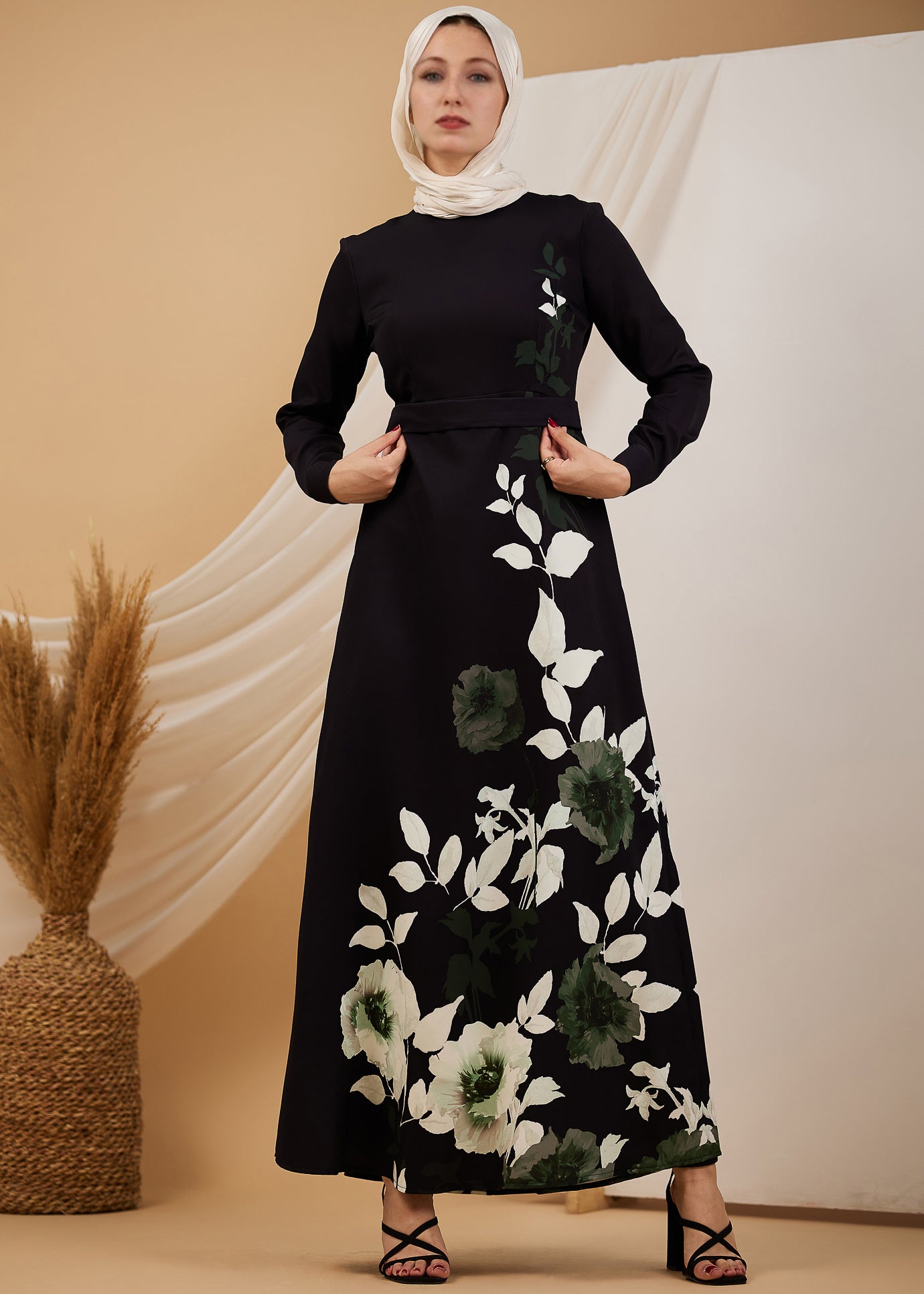 Side view of a black maxi dress with green and white floral designs, worn by a woman in a hijab