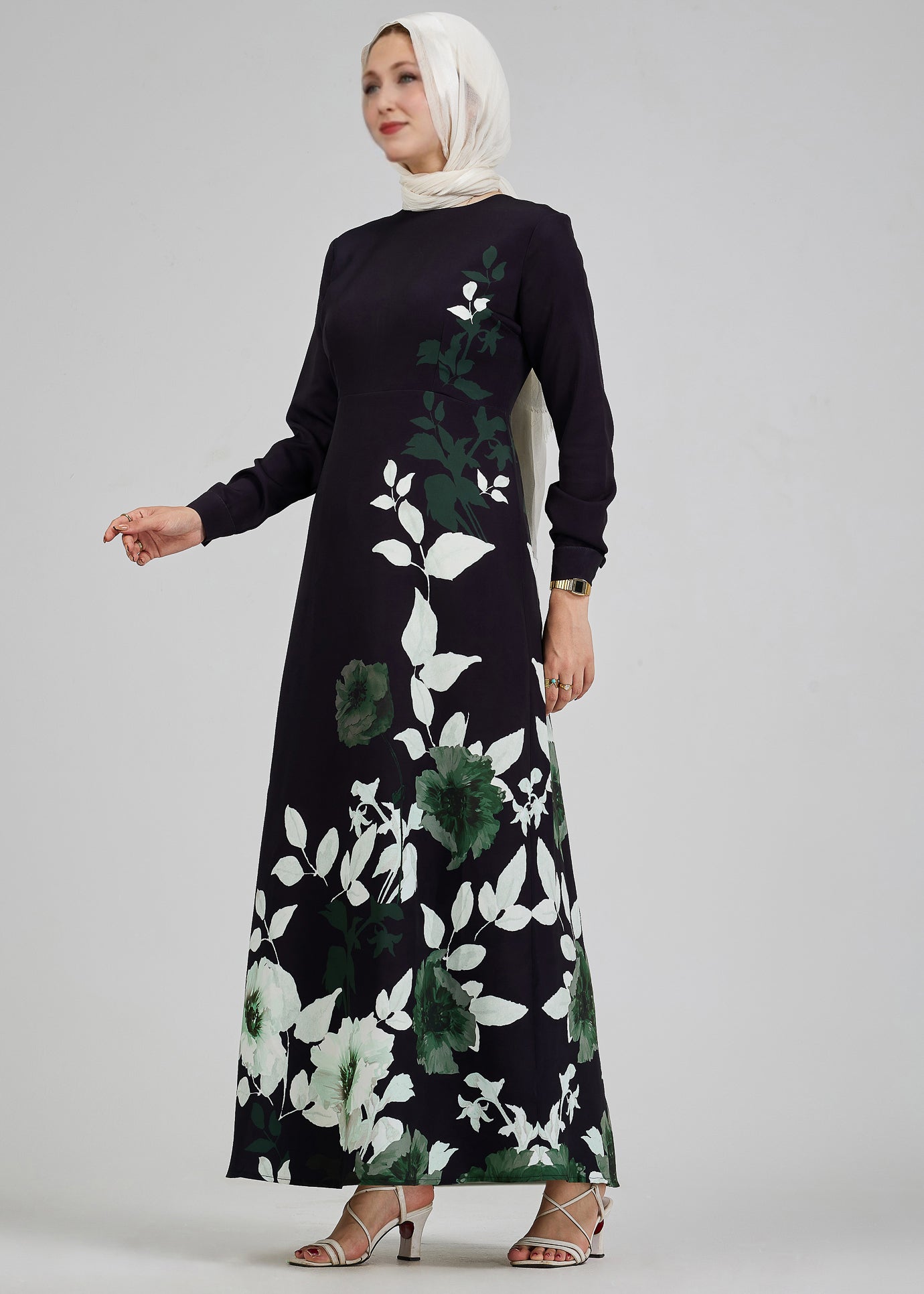 Front view of a woman in a black floral maxi dress with green and white leaf accents, standing gracefully