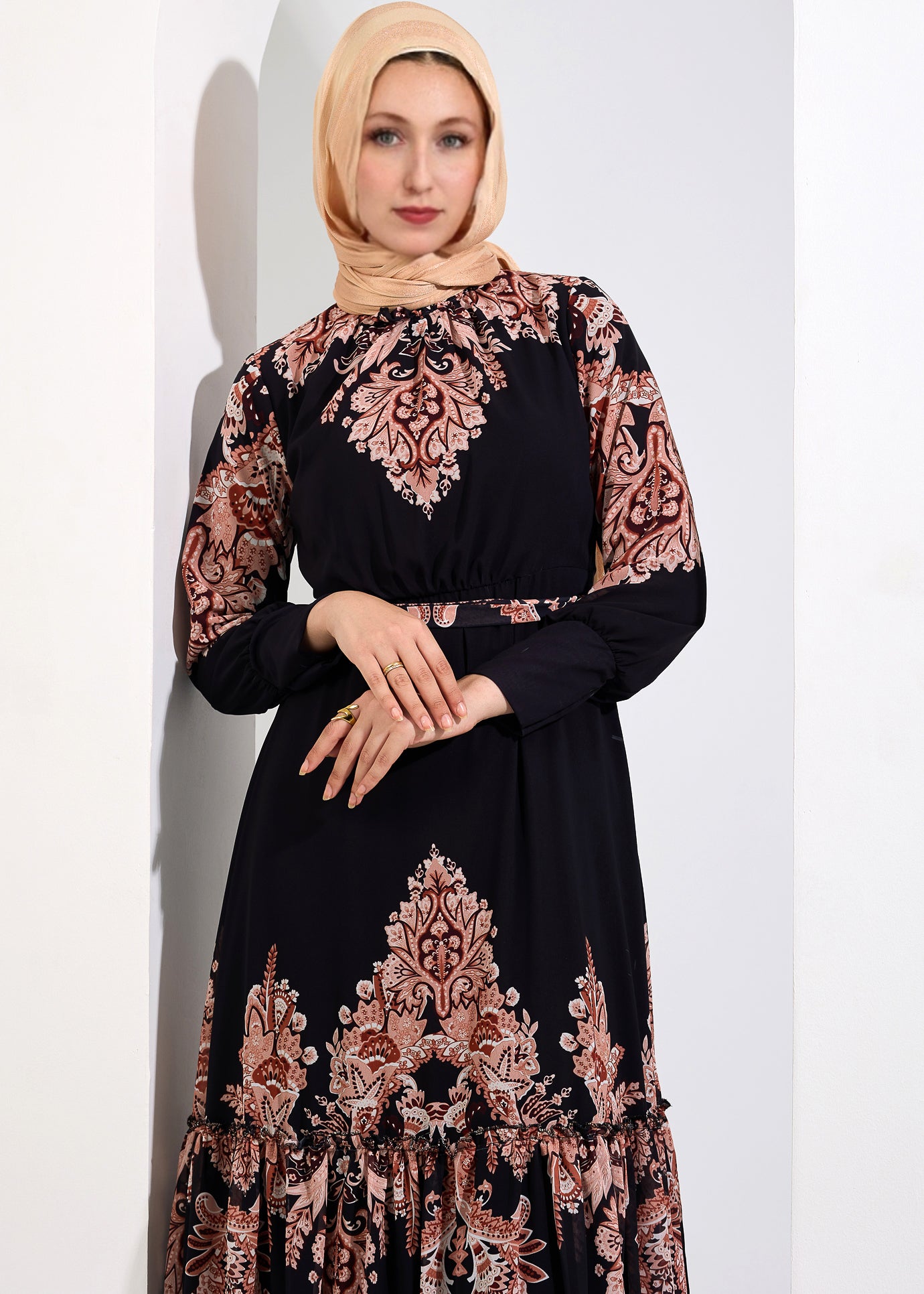 Close-up of a woman in a black chiffon maxi dress with peach floral print, hands clasped