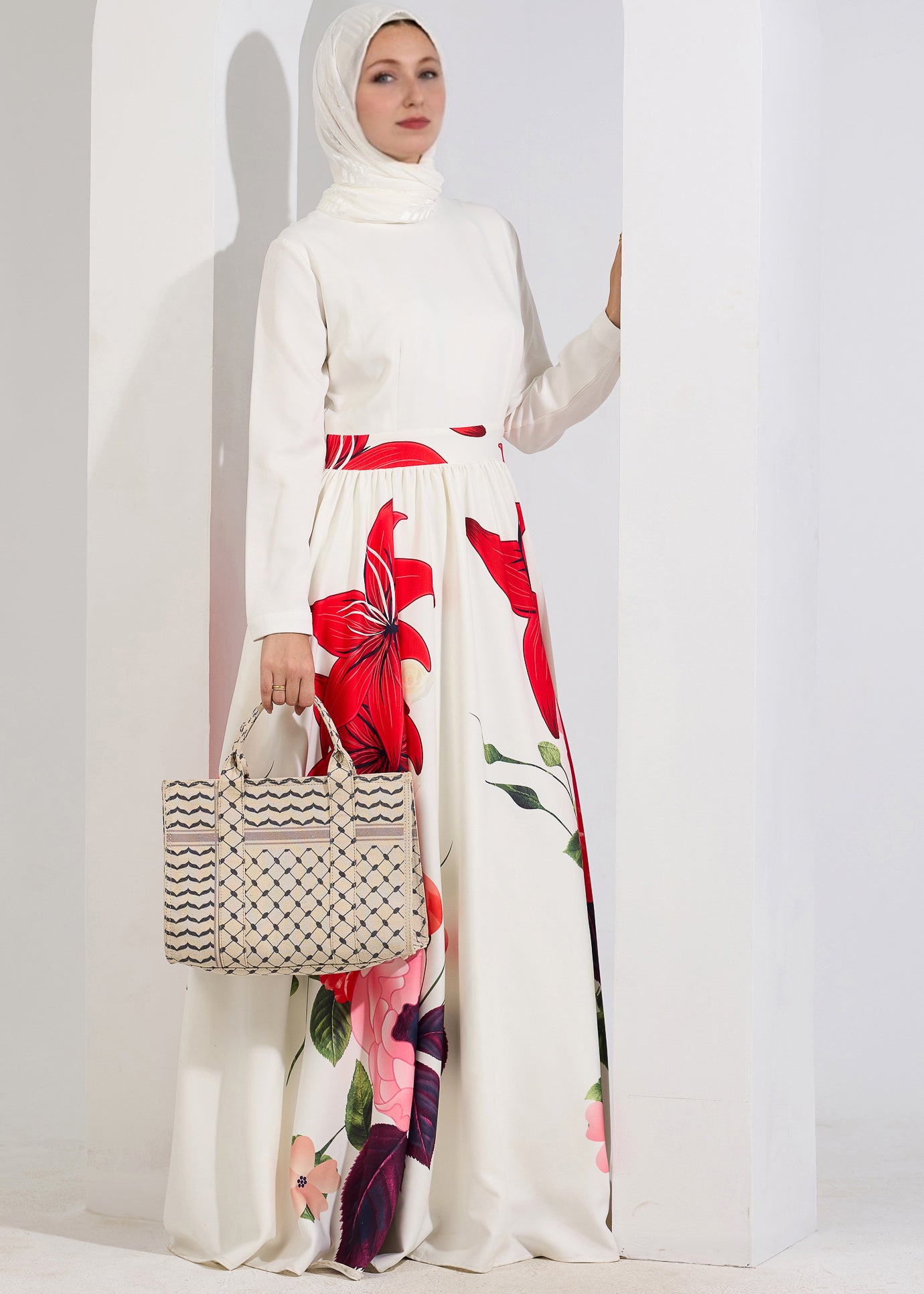 A model posing with a woven bag, dressed in the Radiant Blossom Crepe Maxi Dress with vibrant red floral patterns