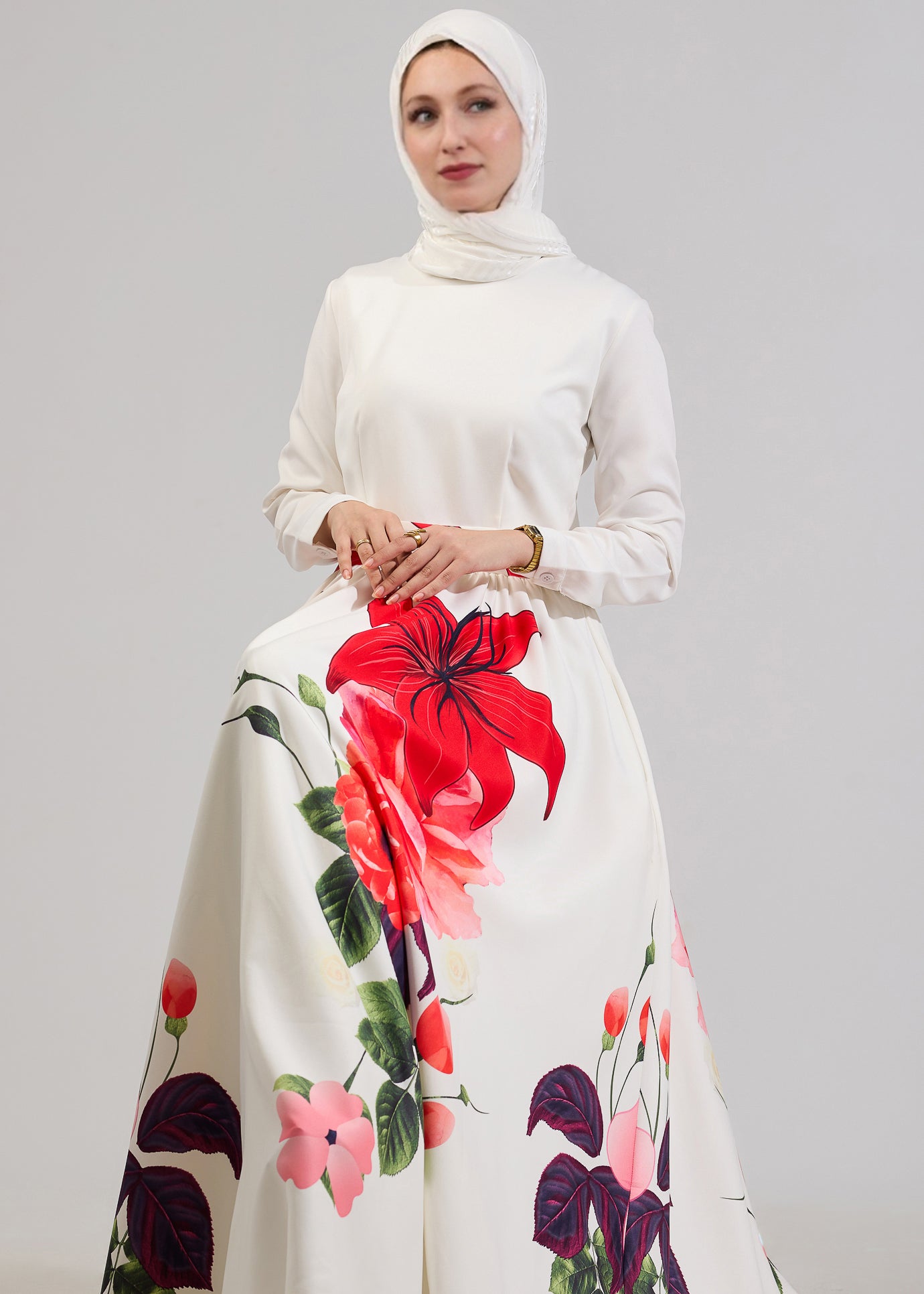 A seated model in the Radiant Blossom Crepe Maxi Dress, showing the intricate red floral design