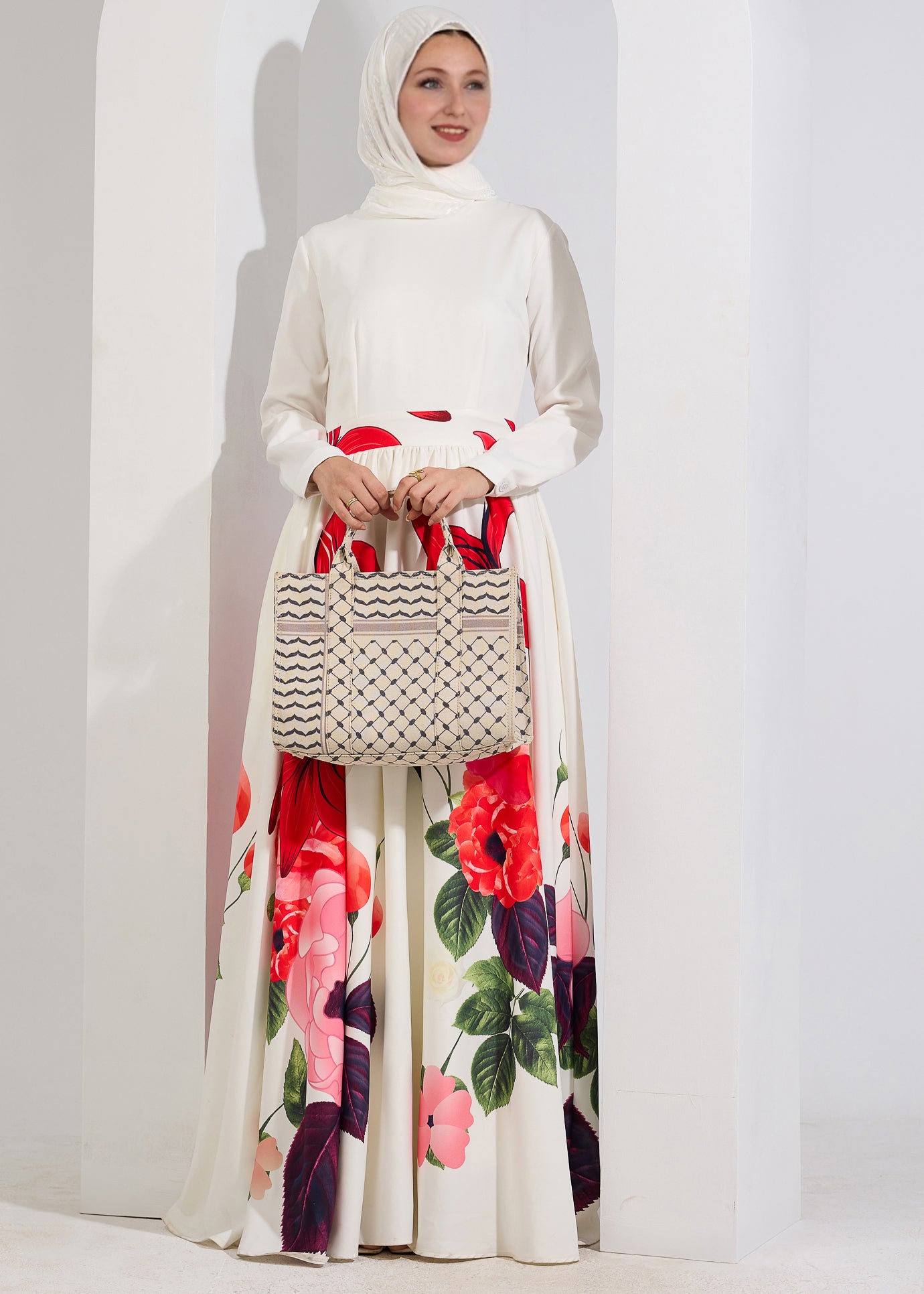 A model holding a woven bag while wearing the Radiant Blossom Crepe Maxi Dress with red floral accents