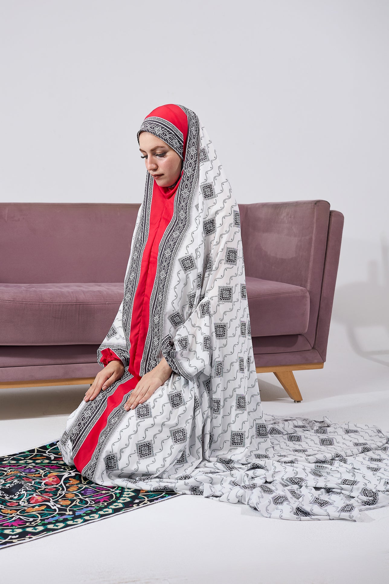 Woman wearing black and white satin prayer gown with red inner layer, seated in prayer