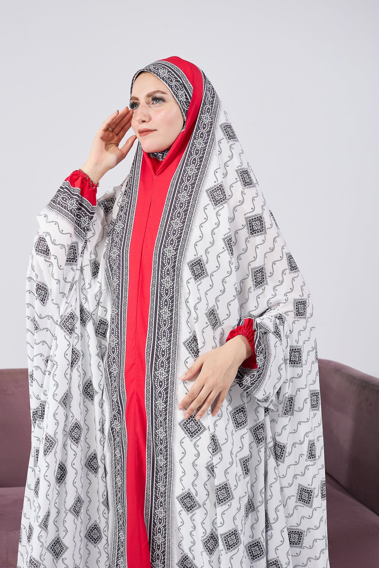 Woman seated in prayer, wearing satin gown with black and white print and red accents